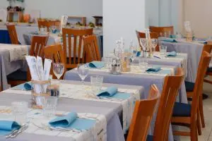Tavoli di un ristorante apparecchiati con tovaglie grigie e tovaglioli azzurri.