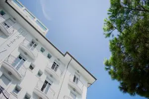 Edificio bianco visto dal basso accanto a un albero e cielo azzurro.