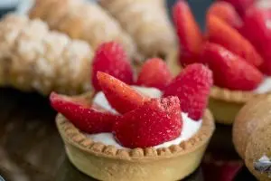 Crostatine alla frutta con fragole fresche su sfondo di dolci assortiti.