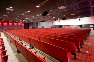 Sala teatrale vuota con file di poltrone rosse e soffitto scuro con faretti