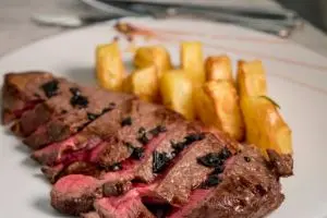 Bistecca di manzo al sangue tagliata a fette con patate fritte al rosmarino su piatto bianco