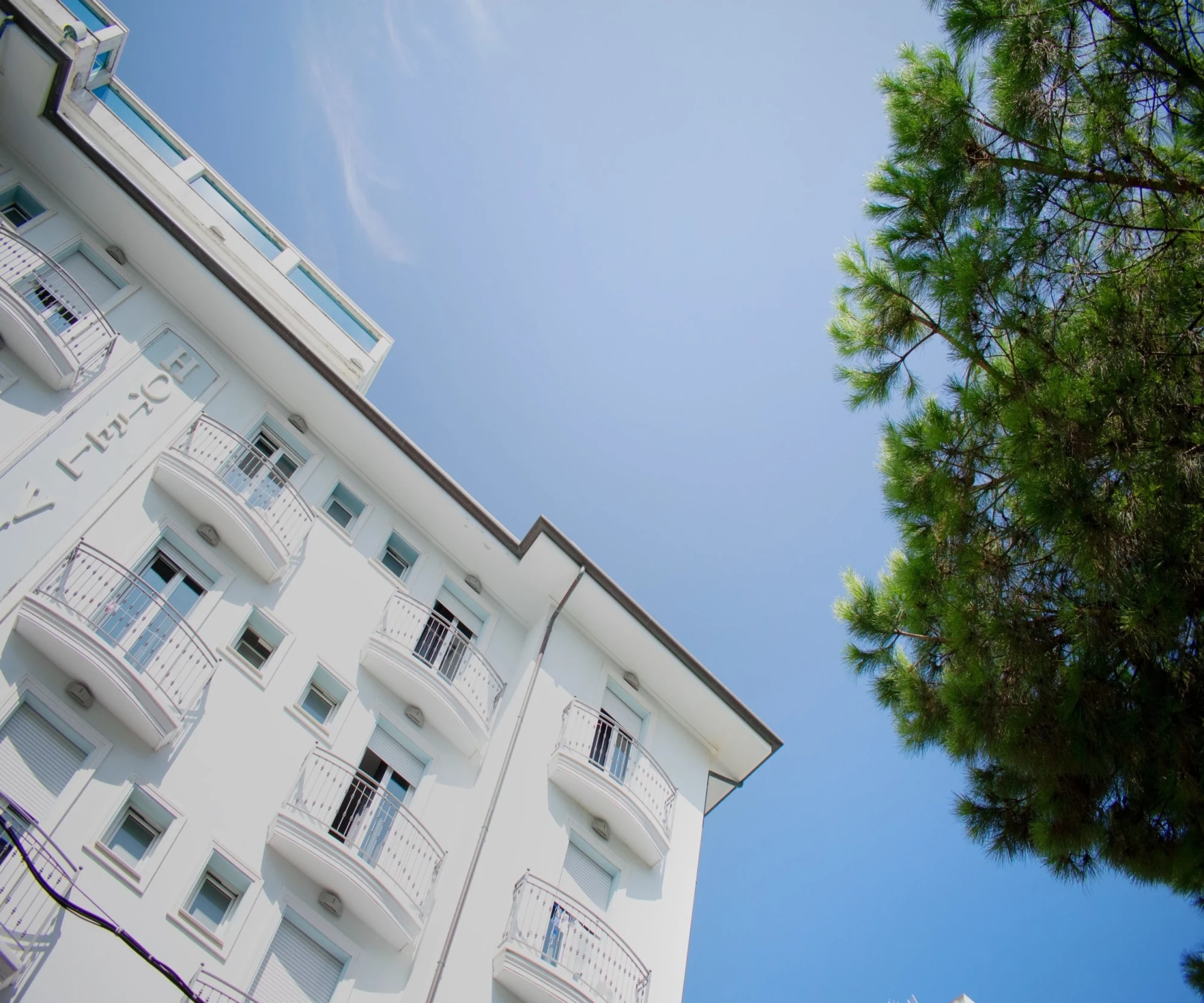 Edificio bianco con balconi e cielo blu con alberi verdi.