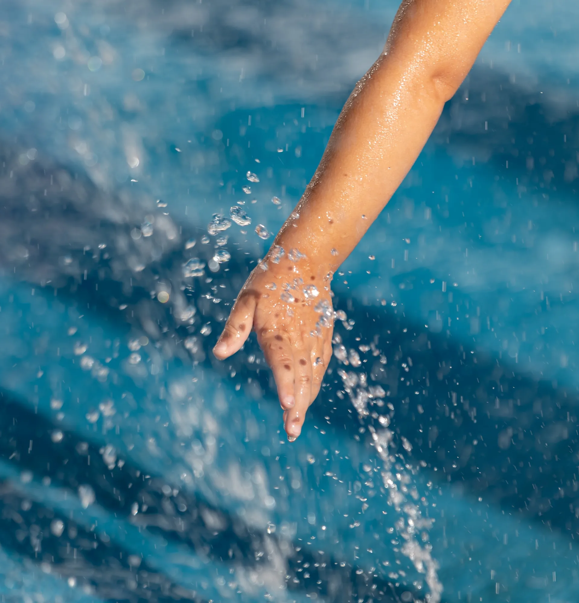 Una mano sfiora l’acqua limpida della piscina sollevando spruzzi