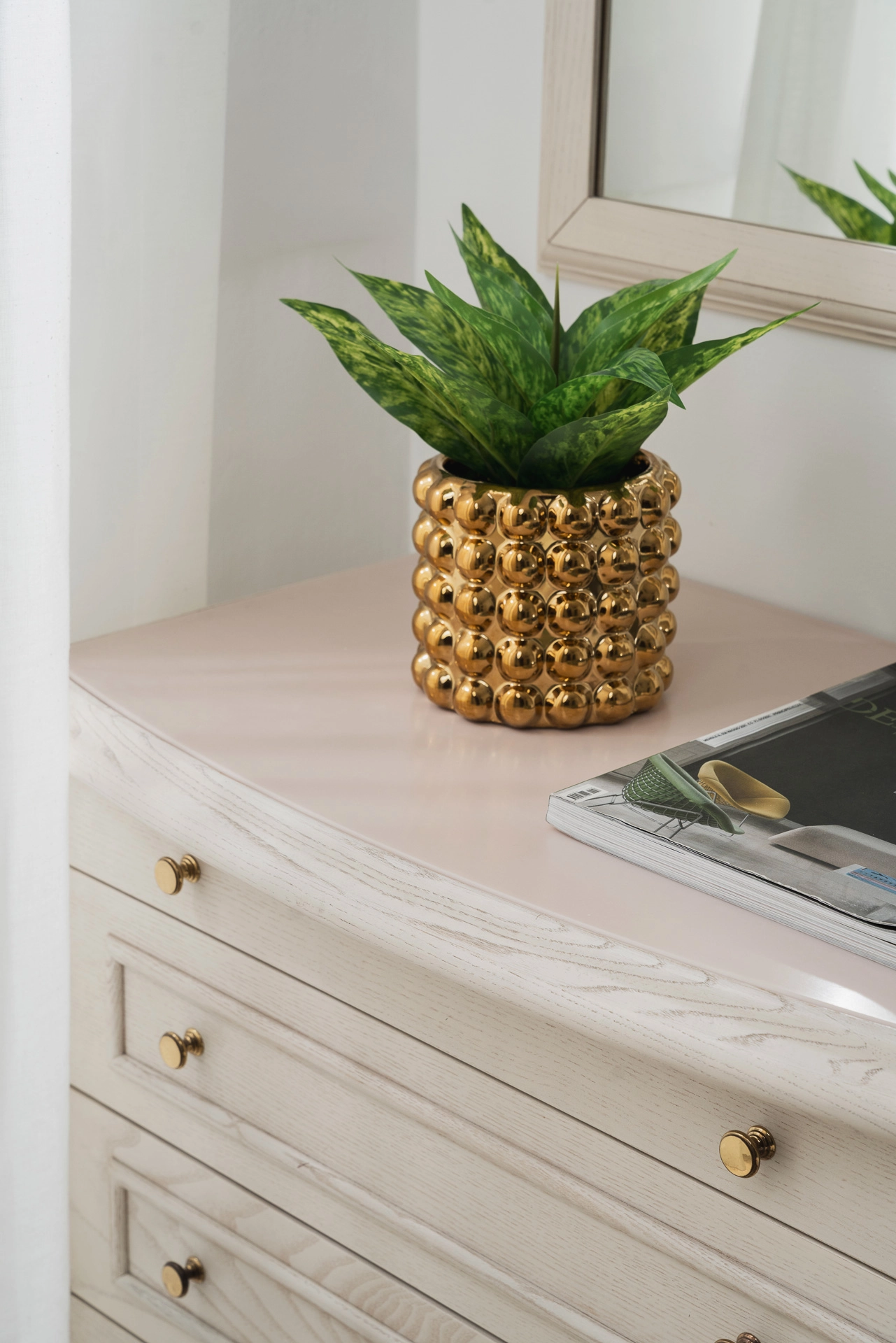 Dettaglio del comò della camera, con vaso dorato a forma di ananas e una pianta