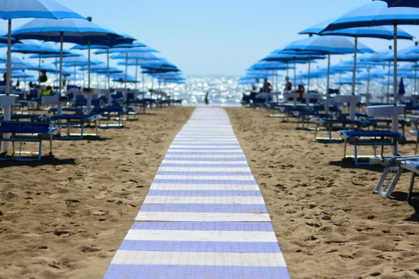 Spiaggia con lettini e ombrelloni blu allineati lungo un camminamento verso il mare.