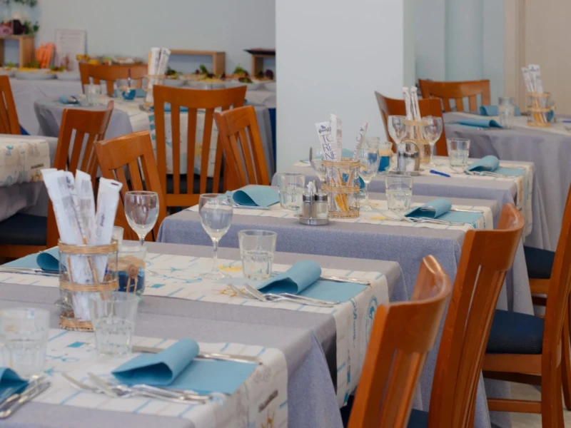 A restaurant with tables set with blue and gray tablecloths, blue napkins, and wooden chairs.