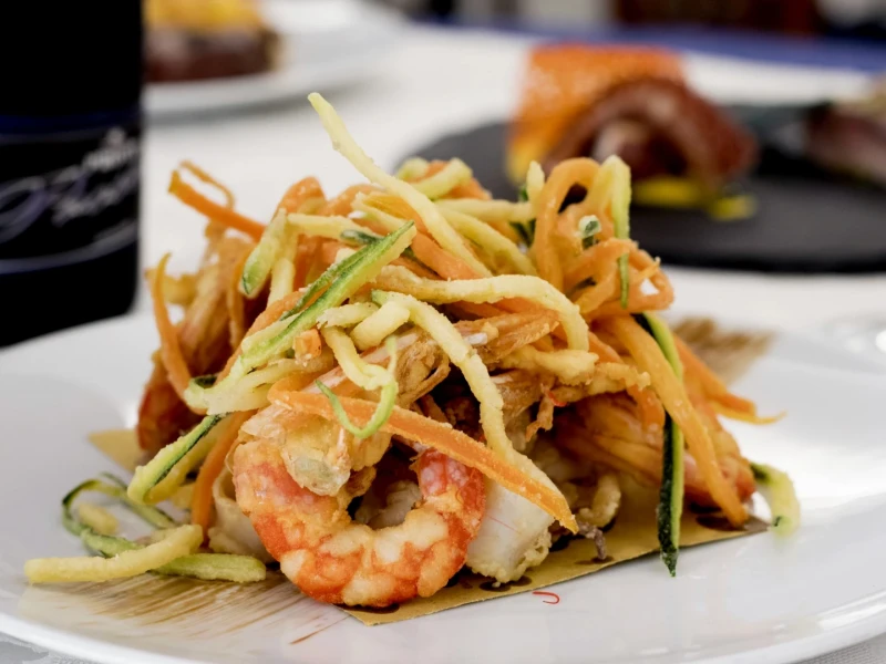 Frittura di gamberi e verdure su un piatto bianco.